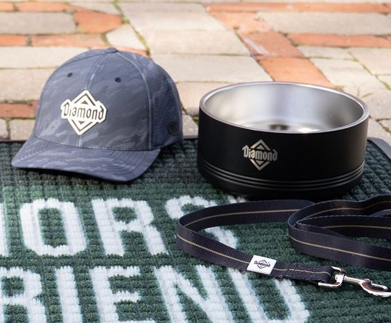 A Diamond branded hat, food bowl and leash lying on a green Warriors' Best Friend rug.
